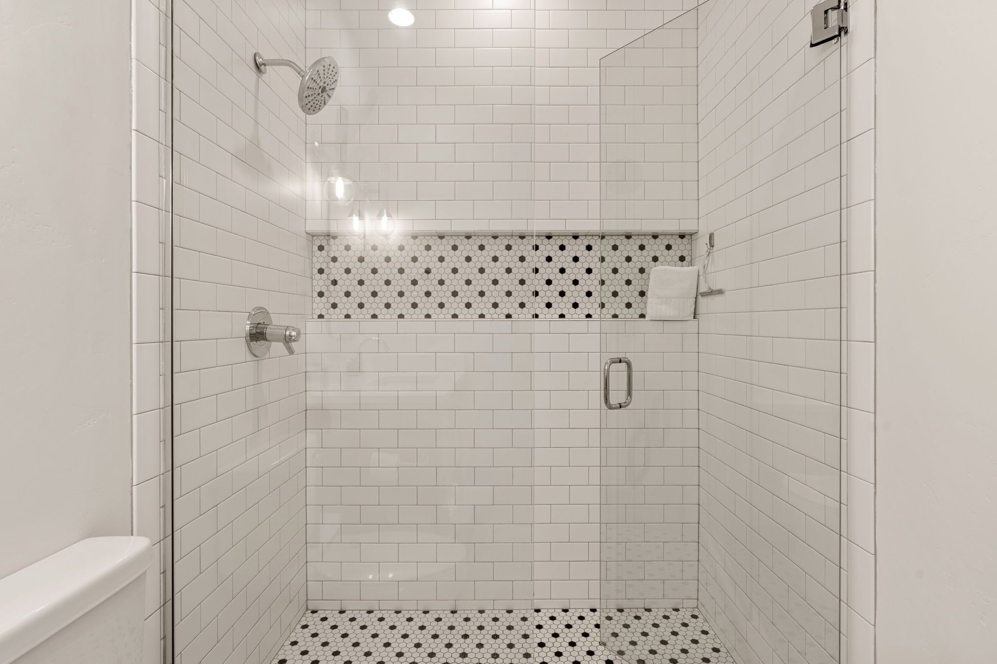 A shower with white tiles, a glass door, and a black and white patterned floor.