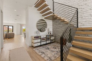 Un interior moderno con una escalera, un espejo redondo, una consola y vistas al exterior.