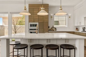 Una cocina moderna con una isla grande, luces colgantes y taburetes de bar.