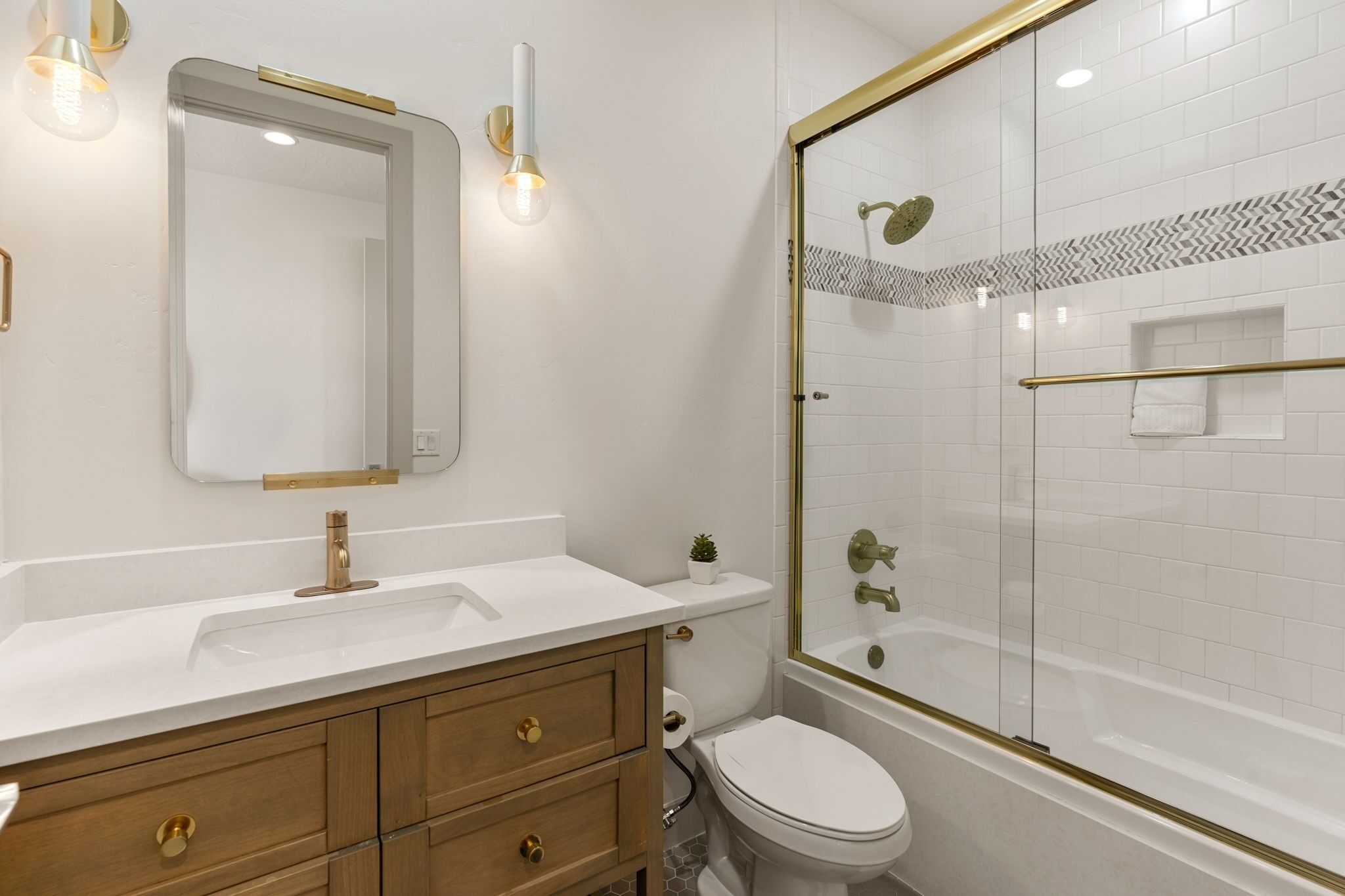 Bagno con lavandino bianco, uno specchio, un water e doccia vetrata con cornice dorata.