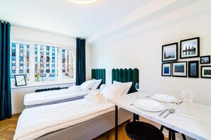 Habitación de hotel con dos camas, una mesa de comedor preparada para dos personas y ventana con vista a la ciudad.