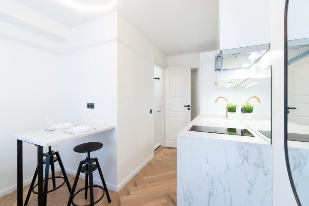 A modern kitchen with a marble countertop, two stools, and a large mirror.