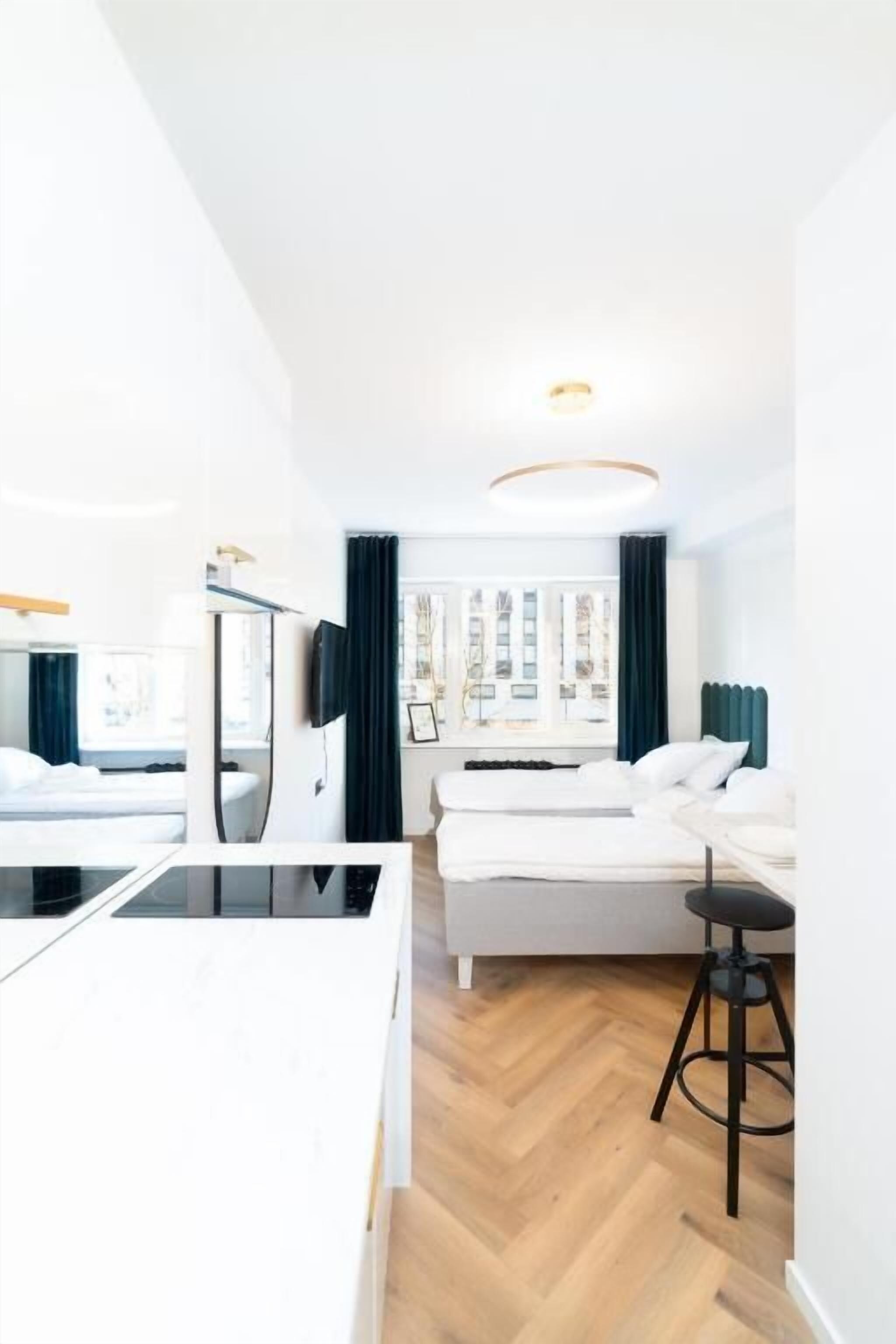 A modern hotel room with a bed, a desk, a chair, a small table, and a view of the city.