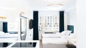 A modern hotel room with a bed, a desk, a chair, a small table, and a view of the city.