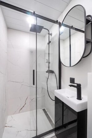 A modern bathroom with a glass-enclosed shower, a white sink, and a round mirror. - Tallinn Airport Studios by RevalHome (Tallinn)