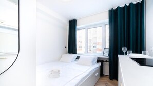 Moderni hotellihuone, jossa on sänky, työpöytä ja ikkuna, jossa on verhot.