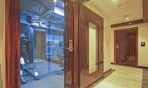 A hotel entrance with a wooden door, a glass door leading to a gym area, and a carpeted hallway. - Dee Empresa Hotel (Kolkata)