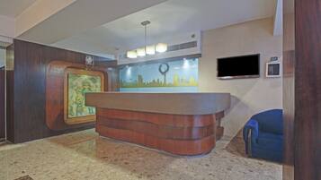 A reception desk with a wooden finish, a wall-mounted flat-screen TV, and a framed picture on the wall.