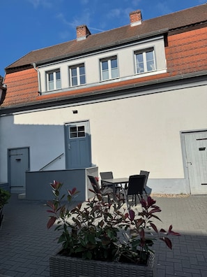 Ein Gebäude mit weißer Fassade, roten Ziegeln und einer kleinen Terrasse mit Tisch und Stühlen.