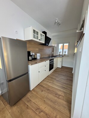 Eine moderne Küche mit einem Edelstahl-Kühlschrank, Holzschränken, einem eingebauten Backofen und einem Fenster mit Aussicht.