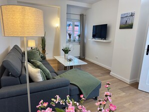 Ein Wohnzimmer mit einer Couch, einem Couchtisch, einer Lampe, einem Fernseher und einem Bild an der Wand.