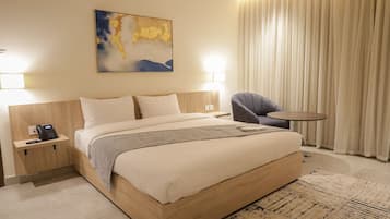 A hotel room with a large bed, a chair, a small table, and a painting on the wall.