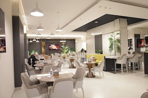 A modern restaurant with round tables, white chairs, and pendant lighting.