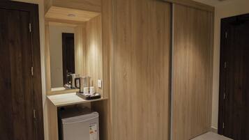 A room with a wooden wardrobe, a small kitchenette with a refrigerator, and a mirror above the counter.