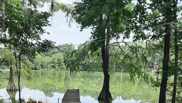 Deux fauteuils Adirondack en bois, placés face à un petit foyer extérieur, avec vue sur un lac et des arbres.