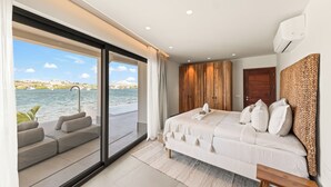 Een slaapkamer met een groot raam, een bed, een houten garderobe en uitzicht op het water.