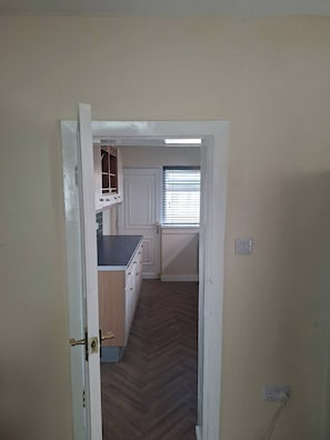 Un pasillo que conduce a una cocina con armarios de madera, una encimera y una ventana con persianas.