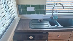 Una cocina compacta con lavadora, lavamanos y ventana con persianas.