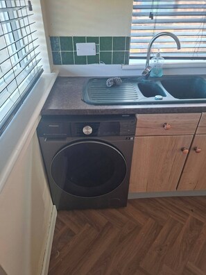 Una cocina compacta con lavadora, lavamanos y ventana con persianas.