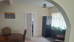 Un comedor con una mesa y sillas, un refrigerador y vistas a un balcón con plantas a través de un vano.