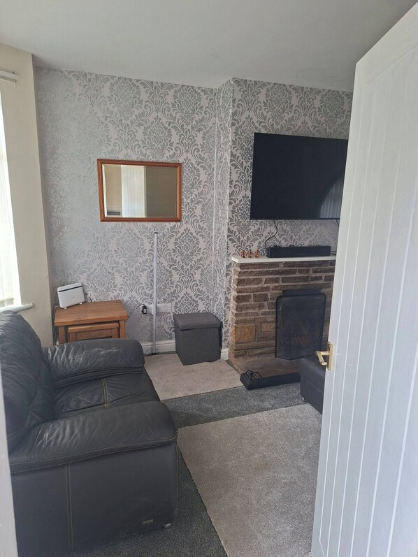 A living room with a sofa, a television mounted on the wall, a fireplace, and a small wooden table.