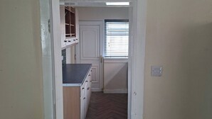Un pasillo que conduce a una cocina con armarios de madera, una encimera y una ventana con persianas.