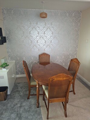A dining area with a round wooden table, four chairs, a decorative wall, and a ceiling light fixture.