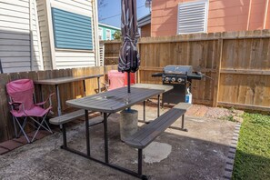 Eine Terrasse mit Tisch, Bänken, einem Grill, einem pinkfarbenen Klappstuhl und einem Betonblock.