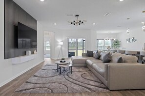 Ein modernes Wohnzimmer mit einem Ecksofa, einem flachbildfernseher an der Wand, einem runden Couchtisch und einem gemusterten Teppich.
