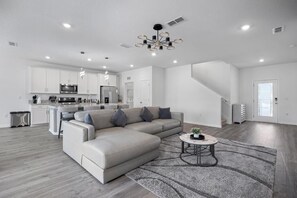 Ein modernes Wohnzimmer mit einer Eckcouch, einem Esstisch und einer Küche im Hintergrund.