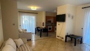 A living room with a sofa, a dining table, and a kitchen area in the background. - Elysia Park Pafos (Paphos)