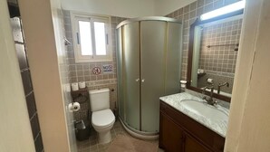 A bathroom with a toilet, shower, sink, and mirror. - Elysia Park Pafos (Paphos)