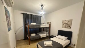 A bedroom with bunk beds, a single bed, a ceiling light, and a door. - Elysia Park Pafos (Paphos)