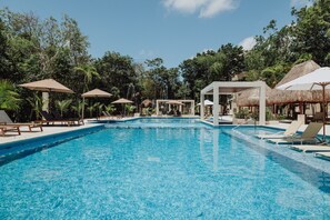 Una piscina con lettini e ombrelloni, circondata da alberi.
