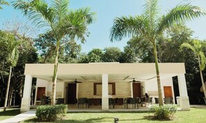 A covered outdoor seating area with chairs and tables, surrounded by palm trees and greenery. - Modern Jungle Escape - Selva Escondida 2
Family sized condo with pool and gym (Puerto Morelos)