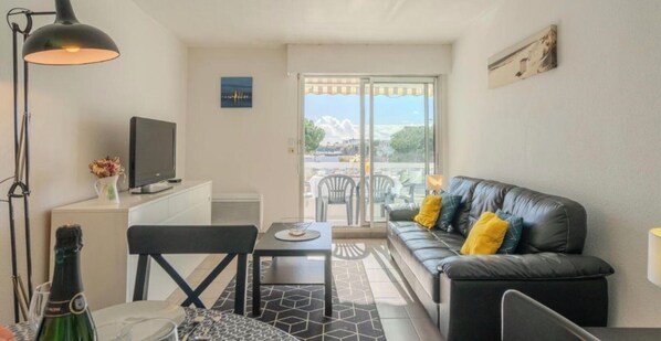 Una habitación moderna con sofá, una mesita, televisor y balcón con vistas.