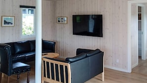 Una sala de estar con un sofá de cuero negro, una mesa de centro de madera y un televisor montado en la pared.