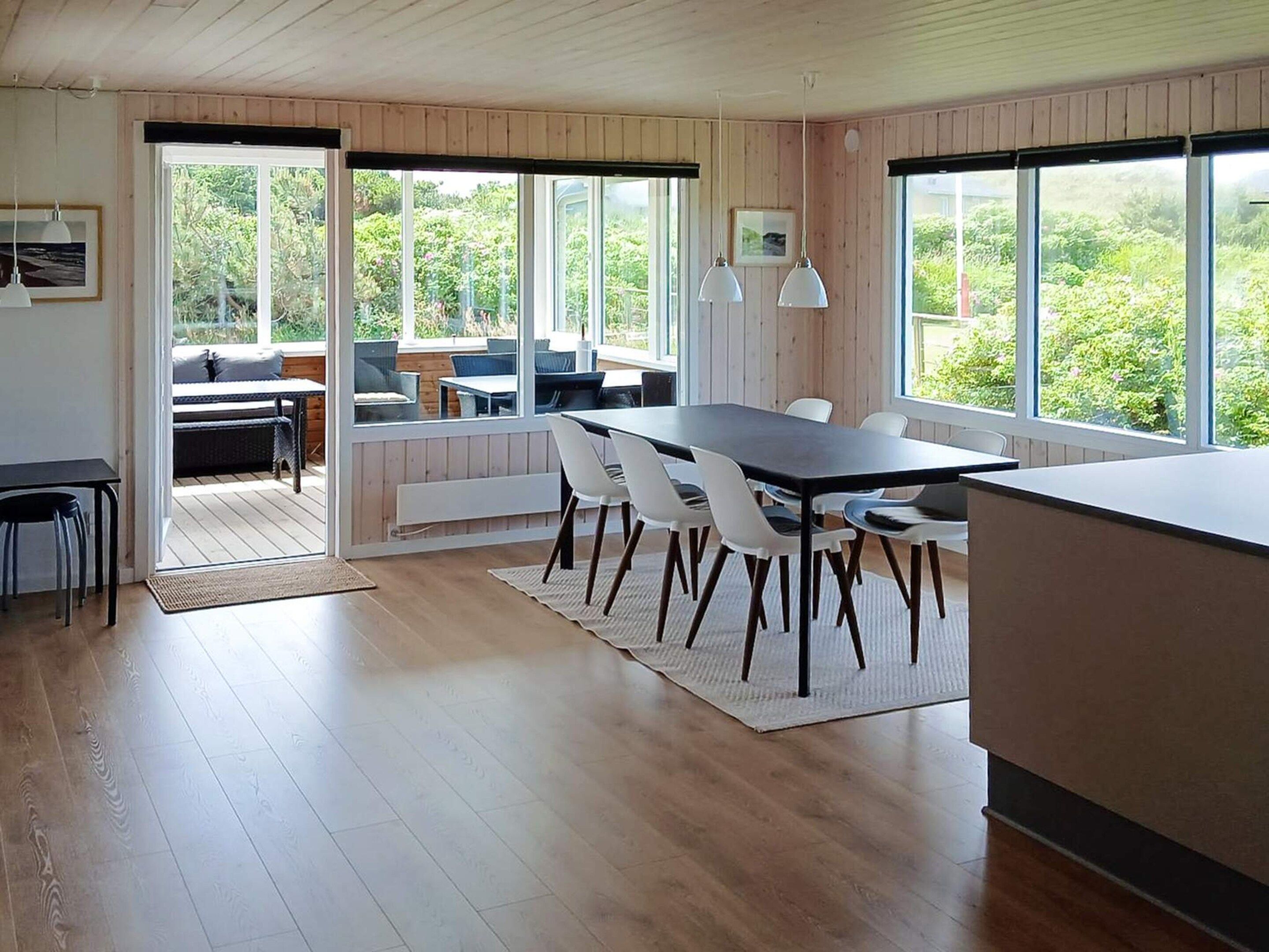 Eine moderne Küche mit Holzboden, einem Essbereich mit Tisch und Stühlen und großen Fenstern mit Blick ins Grüne.