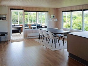 Eine moderne Küche mit Holzboden, einem Essbereich mit Tisch und Stühlen und großen Fenstern mit Blick ins Grüne.