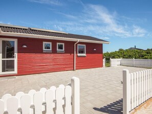 A red building with a tiled patio, white picket fence, and a clear sky. - 4 Star Holiday Home in Ringkobing (Ringkobing)