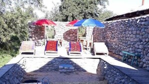 A swimming pool with lounge chairs and umbrellas, surrounded by stone walls. - Belzhan Yurt Lodge (Grigorevka)