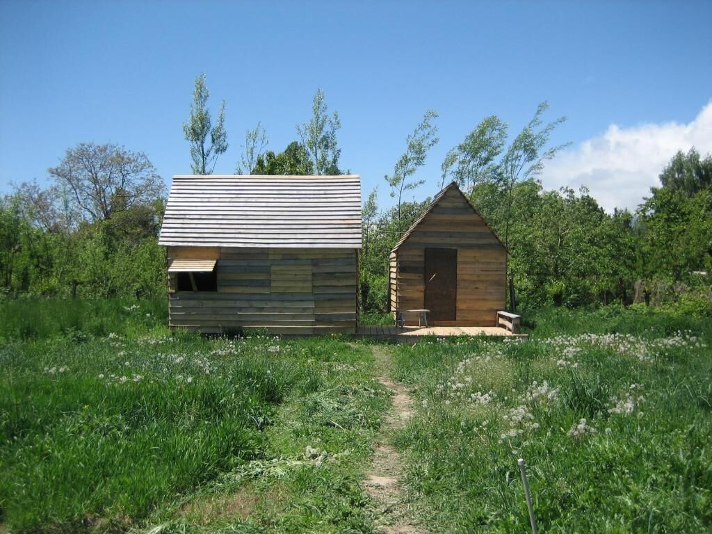 Two wooden cabins in a grassy field with a clear sky.