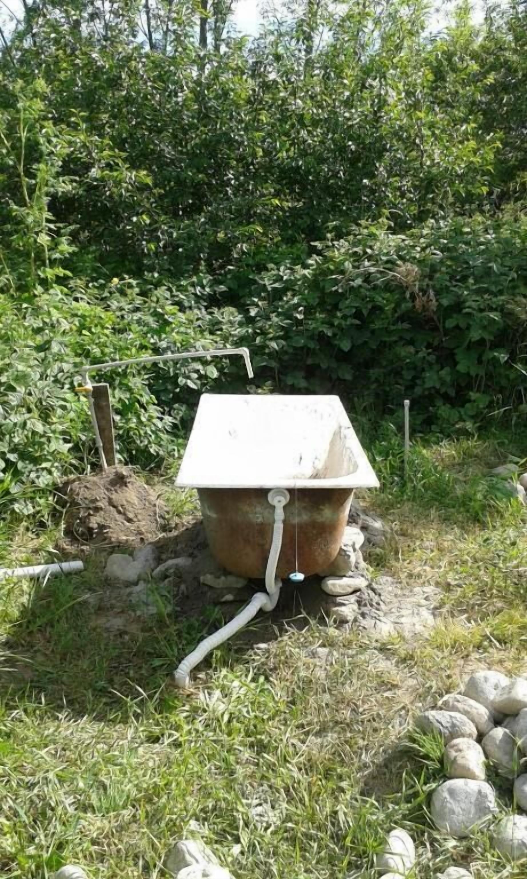 Un baño exterior rústico con estructura metálica, asiento blanco y manguera unida al lateral.