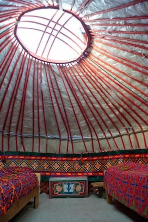 A yurt interior with a circular ceiling, two beds, and a central decorative table.