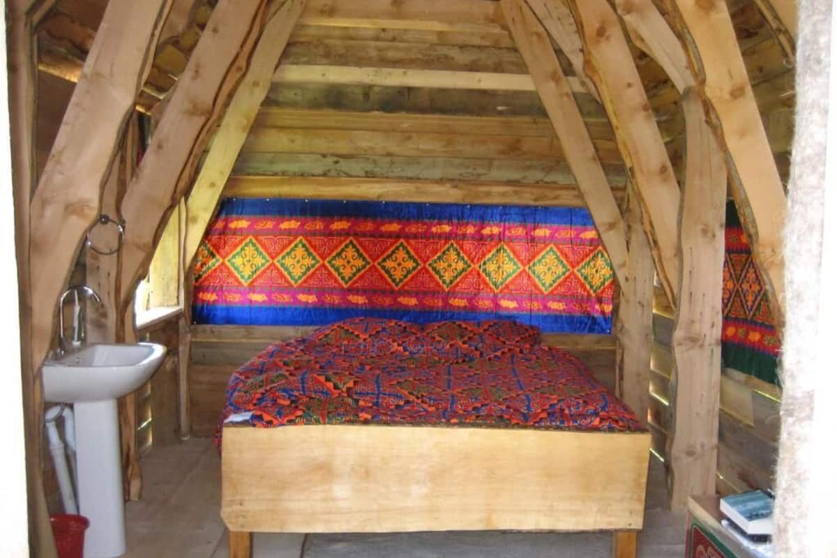 Una habitación con techo de madera, una cama con un edredón colorido, un lavabo y un mueble pequeño.