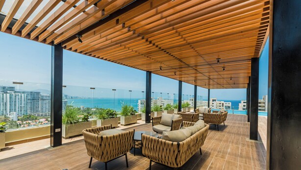 Eine Dachterrasse mit Holzboden, Sitzgelegenheiten im Freien und Blick auf das Meer und die Stadtlandschaft.