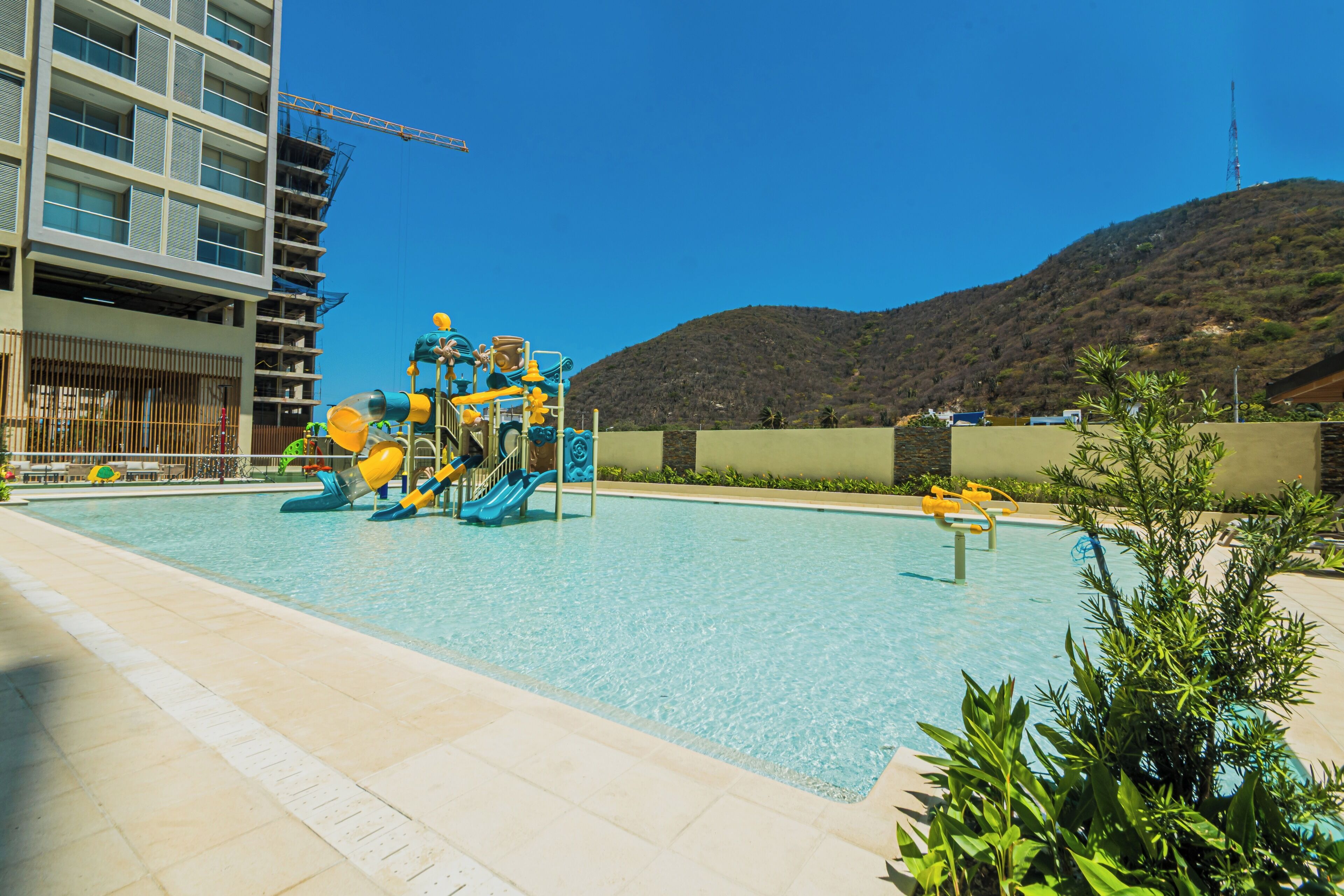 Una piscina con tobogán y un edificio con una grúa de construcción al fondo.