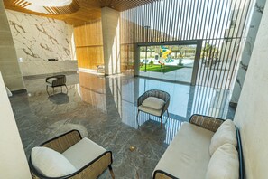 Eine geräumige Lobby mit Marmorboden, Korbmöbeln und Blick auf einen Spielplatz im Freien.