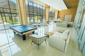 Ein geräumiger Innenbereich mit Billardtisch, Sofas und Blick auf einen Spielplatz durch große Fenster.