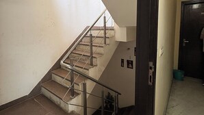 A staircase with metal railings, a door with a handle, and a wall with a light switch. - Staylo Jaggannath Stays (New Delhi)